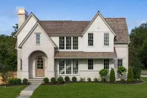 A modern farmhouse-style home with a light stucco exterior, wood accents, and a green lawn.